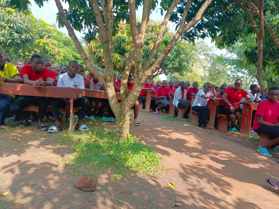 Students gathered on benches outdoors under a tree during a TVIA community education session